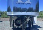 Front view of a blue Merhow horse trailer with its logo, parked on a gravel lot under a clear blue sky