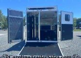 Open aluminum horse trailer with ramp down, interior stalls and tie rails visible in a sunny outdoor lot.