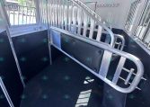 Interior of a silver horse trailer showing a central divider, aluminum rails, and window bars along the walls for ventilation and separation of stalls.