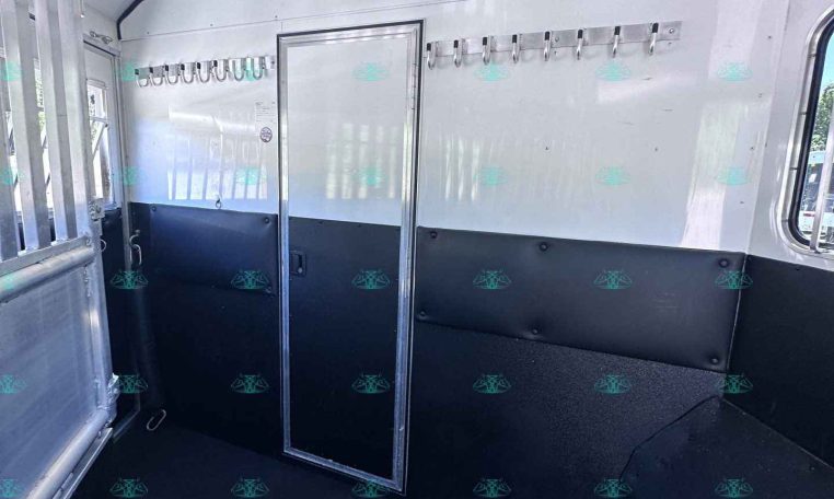 Interior of a light trailer with two rows of metal hooks along the walls and a central door, black cushioned lower walls, and windows visible