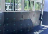 Inside a horse trailer: barred windows along the wall, white interior, and a dark padded divider along the lower wall.