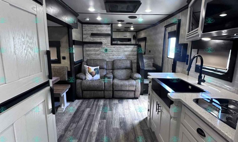 Bright RV interior with white cabinetry, gray sofa, and wood-look flooring across the space.
