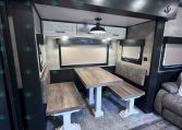 Interior of a camper trailer dining alcove with a wood table, cushioned bench seats, and an overhead light.