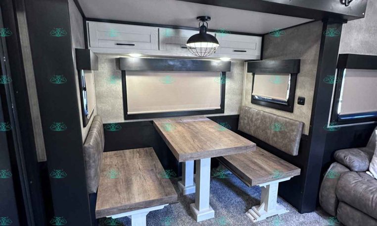 Interior of a camper trailer dining alcove with a wood table, cushioned bench seats, and an overhead light.