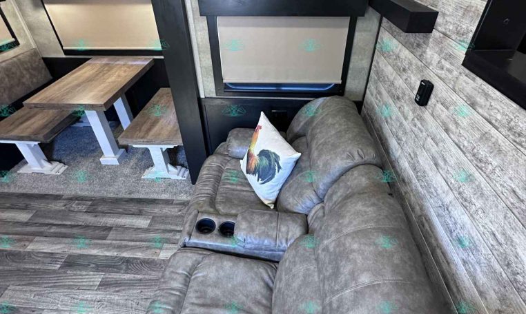 Cozy trailer living area with a gray sectional sofa, a wood dining table with benches, and wood-style walls.