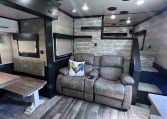 Interior of a modern trailer living area with a gray sofa, rooster pillow, and wood-tone flooring