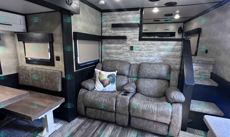 Interior of a modern trailer living area with a gray sofa, rooster pillow, and wood-tone flooring