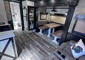 Cozy RV living area with a wooden dining table and bench seating, a sofa with a rooster pillow, and doorway to a bathroom.