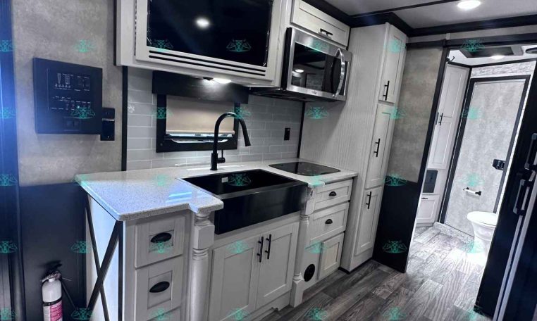 Modern RV kitchen: white cabinets, stainless steel microwave, and a black sink with a curved faucet; light gray subway backsplash and island counter.