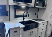RV kitchen with gray cabinets, stainless microwave above stove, and a modern black faucet over a double sink.