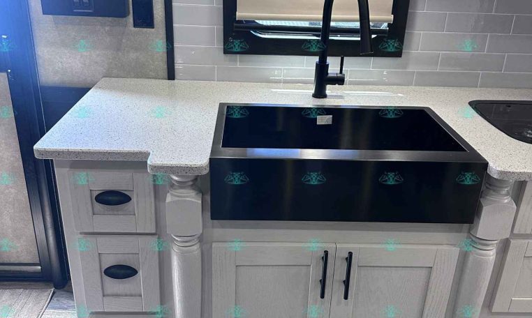 Compact kitchen area in a trailer with a black undermount sink, matte black faucet, light gray cabinets, and a gray tile backsplash across the counter edge.