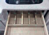 Two-burner gas cooktop under a glass cover set in a speckled countertop, with an empty wooden drawer pulled out underneath.