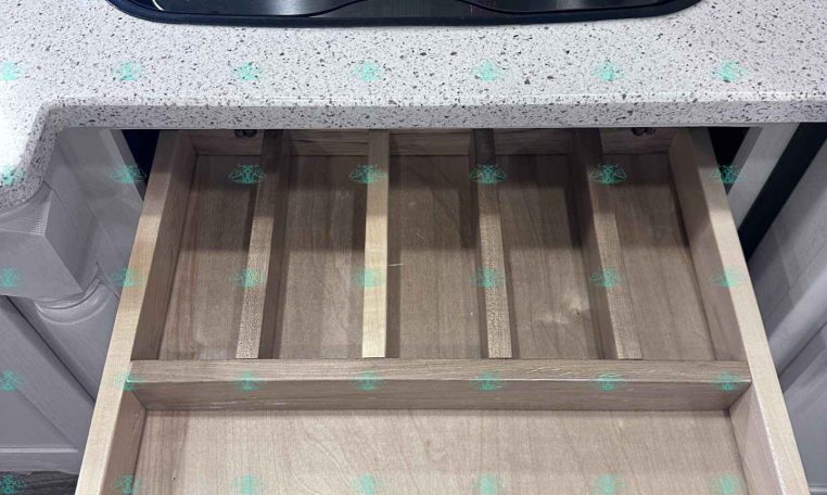 Two-burner gas cooktop under a glass cover set in a speckled countertop, with an empty wooden drawer pulled out underneath.