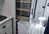 RV kitchen interior with a pull-out wooden pantry shelving unit beside a countertop and sink area in view.