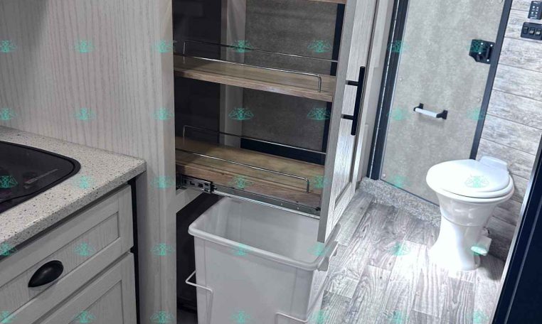 RV kitchen interior with a pull-out wooden pantry shelving unit beside a countertop and sink area in view.