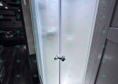 Curved corner shower with frosted glass doors and chrome handle in a compact trailer bathroom