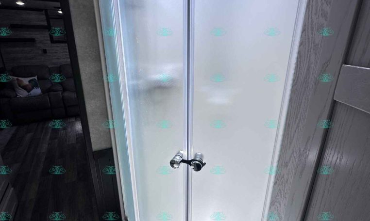 Curved corner shower with frosted glass doors and chrome handle in a compact trailer bathroom