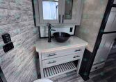 Grey bathroom vanity with mirrored medicine cabinets above a speckled countertop and a black vessel sink; a white toilet is in the foreground.