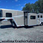 Silver gooseneck horse trailer with living quarters parked on a gravel lot, trees in the background.