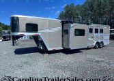 Silver gooseneck horse trailer with living quarters parked on a gravel lot, trees in the background.