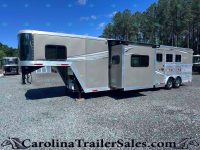 Silver gooseneck horse trailer with living quarters parked on a gravel lot, trees in the background.