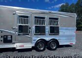 Silver Merhow aluminum horse trailer with three barred stall windows and chrome trim, parked on gravel under a blue sky.