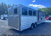 Silver Merhow horse trailer with multiple windows parked on a gravel lot, trees in the background.