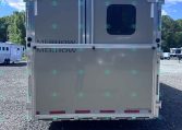 Rear view of a metal horse trailer with a small rounded window and dual doors, parked on gravel under a blue sky.