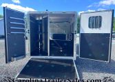 Open horse trailer interior with a divider, lowered ramp, and tack hooks along the left wall.