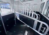 Interior of a aluminum horse trailer with a ramp, divider gate, and stair-style incline for loading horses; black rubber flooring and metal walls visible.