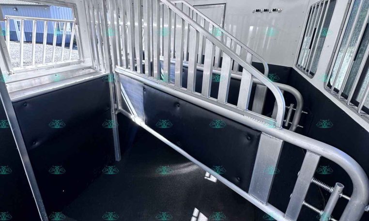 Interior of a aluminum horse trailer with a ramp, divider gate, and stair-style incline for loading horses; black rubber flooring and metal walls visible.