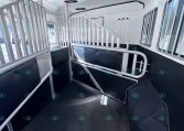 Interior of a metal horse trailer with divider stalls, gray rails, and black padded walls along the sides, ready for horses to ride.
