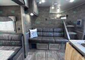 Interior of a modern RV living area with a gray sofa, cabinets, and bunk bed access stairs to a loft/bedroom.