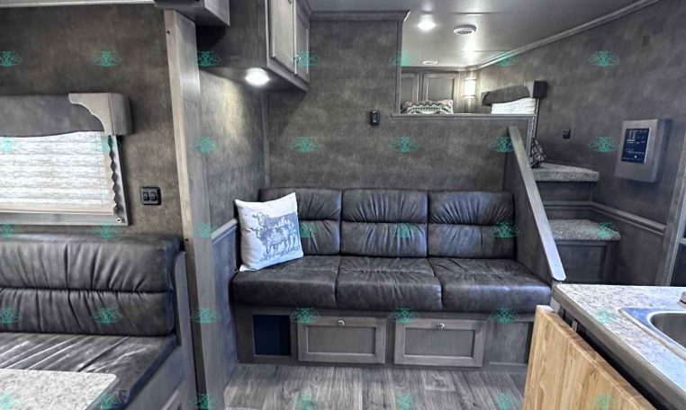 Interior of a modern RV living area with a gray sofa, cabinets, and bunk bed access stairs to a loft/bedroom.