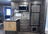 RV kitchen with stainless steel fridge and microwave, gray cabinets, and a wood cutting-board island.