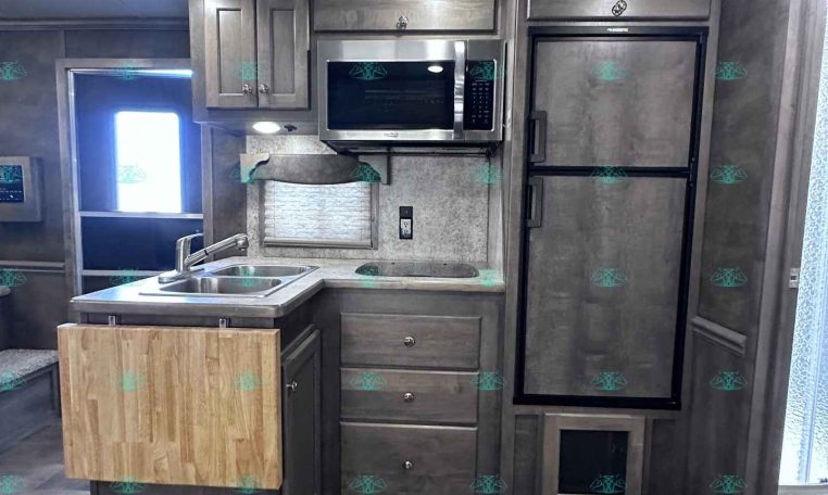RV kitchen with stainless steel fridge and microwave, gray cabinets, and a wood cutting-board island.