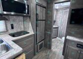 Modern RV kitchen with stainless steel microwave and side-by-side fridge, gray cabinetry, and a countertop stove area.