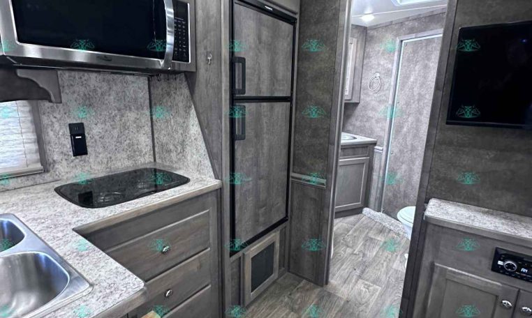 Modern RV kitchen with stainless steel microwave and side-by-side fridge, gray cabinetry, and a countertop stove area.