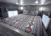 Bedroom inside a travel trailer with a geometric quilt and two pillows against gray wall panels
