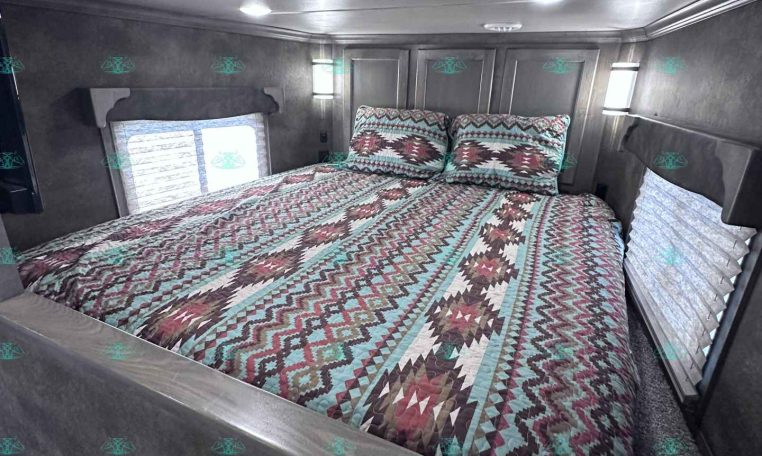 Bedroom inside a travel trailer with a geometric quilt and two pillows against gray wall panels