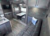 Cozy gray-toned RV living area with dinette, sofa, and wall-mounted TV beneath overhead cabinets in a compact trailer.