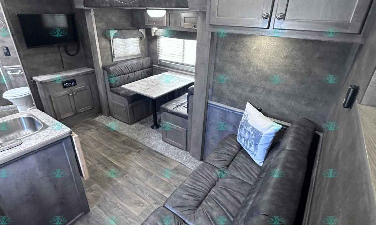 Cozy gray-toned RV living area with dinette, sofa, and wall-mounted TV beneath overhead cabinets in a compact trailer.