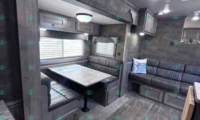 Grey-dominated RV living area with a booth dinette, over-cab bunk, and L-shaped sofa along a corridor of dark wood cabinets and windows.