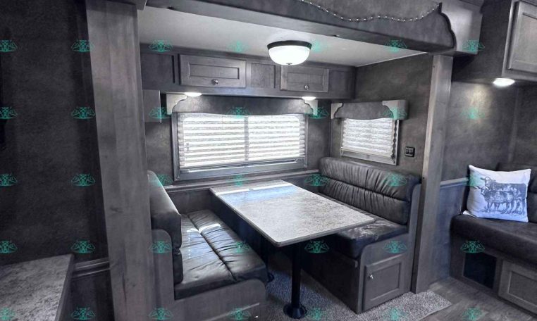 RV dinette with U-shaped gray vinyl bench seating around a rectangular tabletop, string lights above, and cabinets along the wall; windows with blinds in the background.