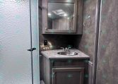 Small bathroom vanity area with gray wood cabinet, oval sink, and mirrored medicine cabinet; frosted glass shower on the left.