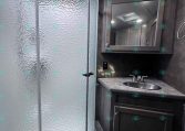 Bathroom inside a trailer: curved glass shower on the left and a dark wood vanity with sink and mirror on the right.