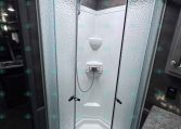 Curved glass shower enclosure in a small RV bathroom with textured frosted doors and a skylight above.