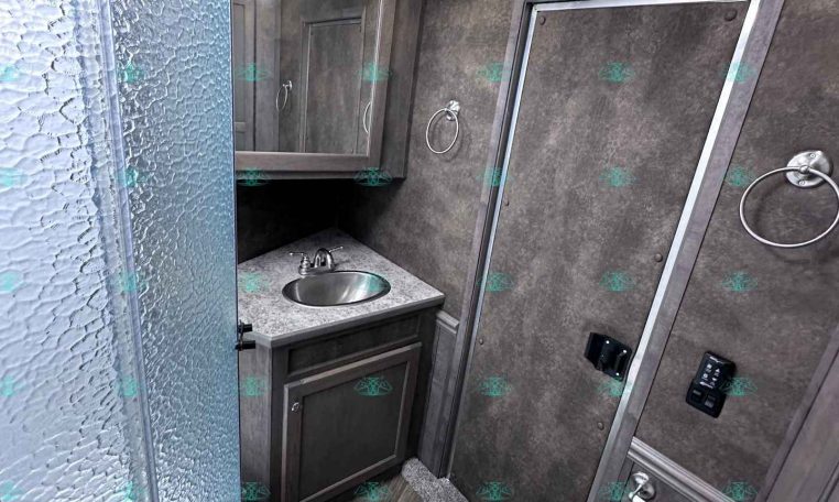 Compact RV bathroom with a frosted glass shower, gray vanity with sink, mirror cabinet, and a toilet in a small trailer interior.
