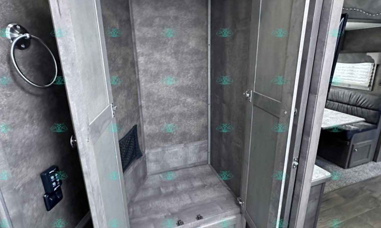 Dark wood trailer bathroom with open cabinet showing a metal rod for hanging clothes; toilet visible in the foreground.