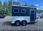 Dark blue travel trailer with two rectangular windows and a side door, parked on gravel with trees in the background.